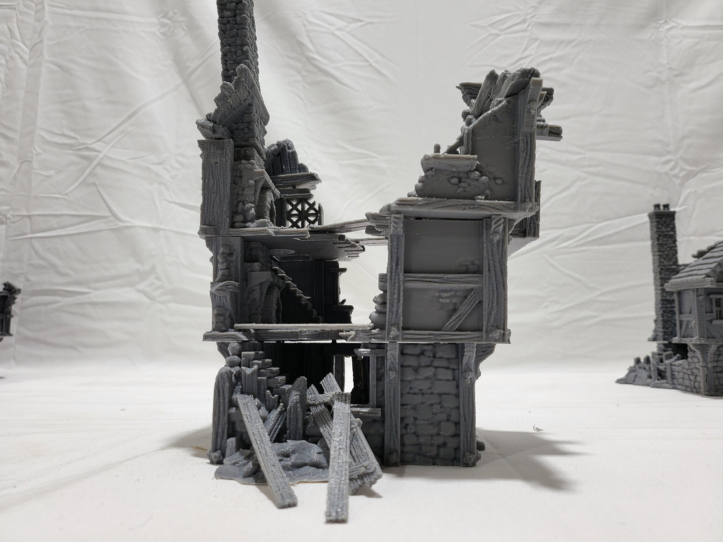 three intricately detailed ruined buildings and a towering structure, showcasing crumbling stone walls, exposed beams, and a hauntingly desolate atmosphere, perfect for bringing medieval and fantasy battles to life on your tabletop.