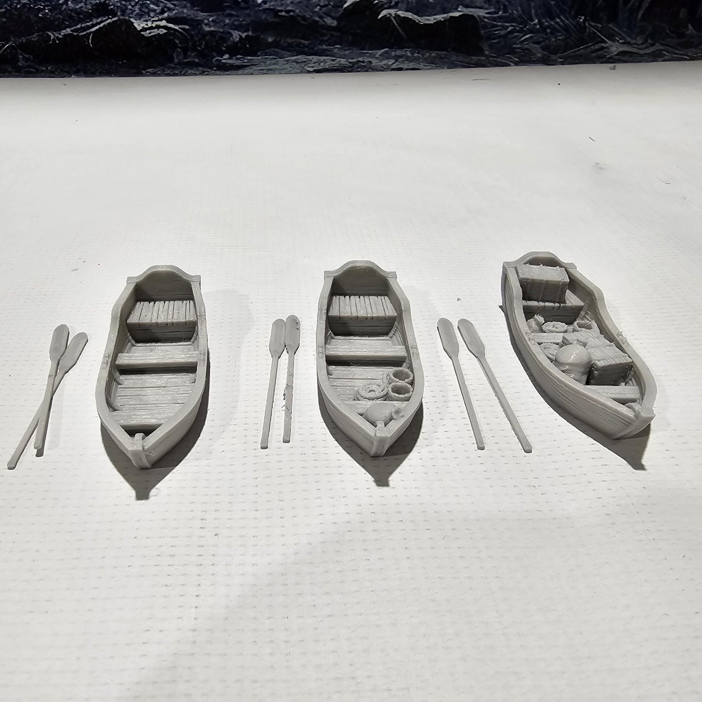 Set of 3 medieval rowboats with crates, barrels, sacks, ropes, and oars. Available in 15mm, 28mm, and 32mm scales—perfect for docks, rivers, and coastal scenes in fantasy and historical tabletop games.