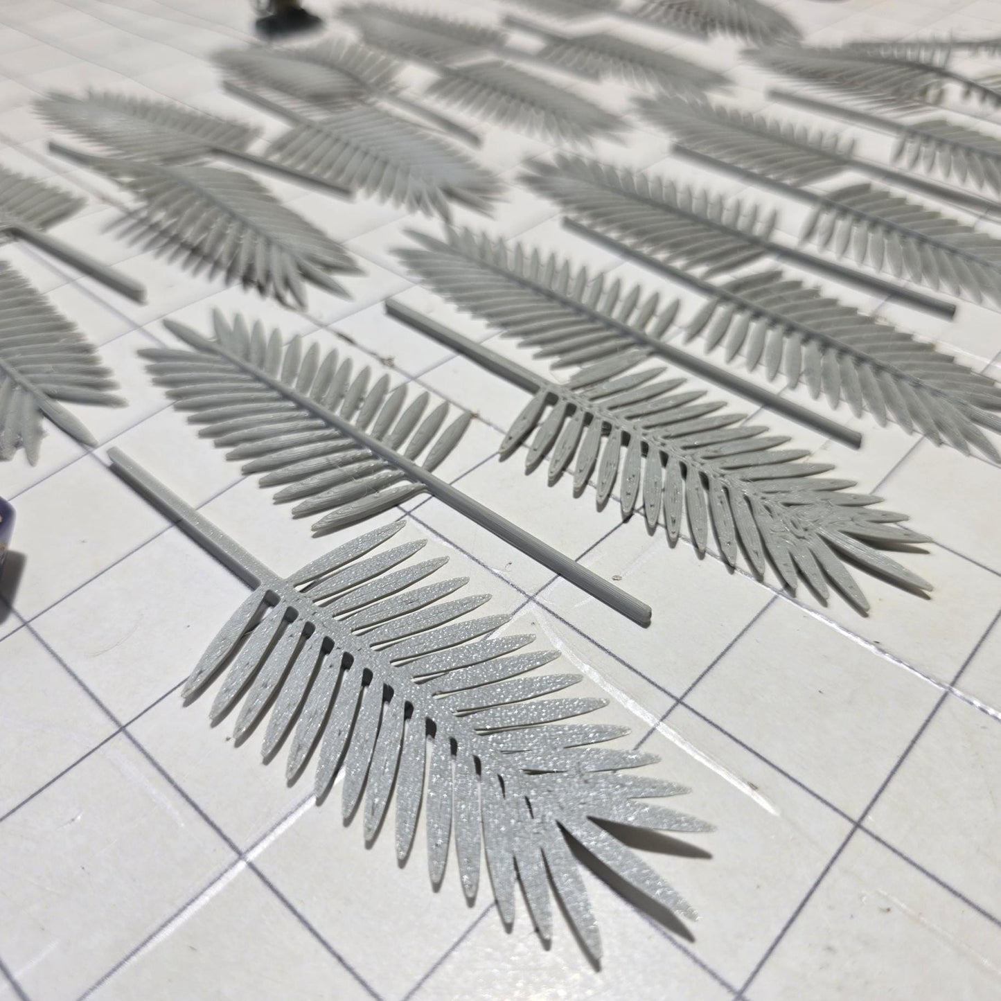 Laid across a 1" grid, these 28mm-scale palm fronds form a tropical spread waiting to be shaped and painted. With identical sprigs that bend under heat, they’re perfect for scratch-building palm trees, decorating temple ruins, or fleshing out dense jungle scenes. A miniature wizard and dice provide a sense of scale, highlighting their table-ready size.