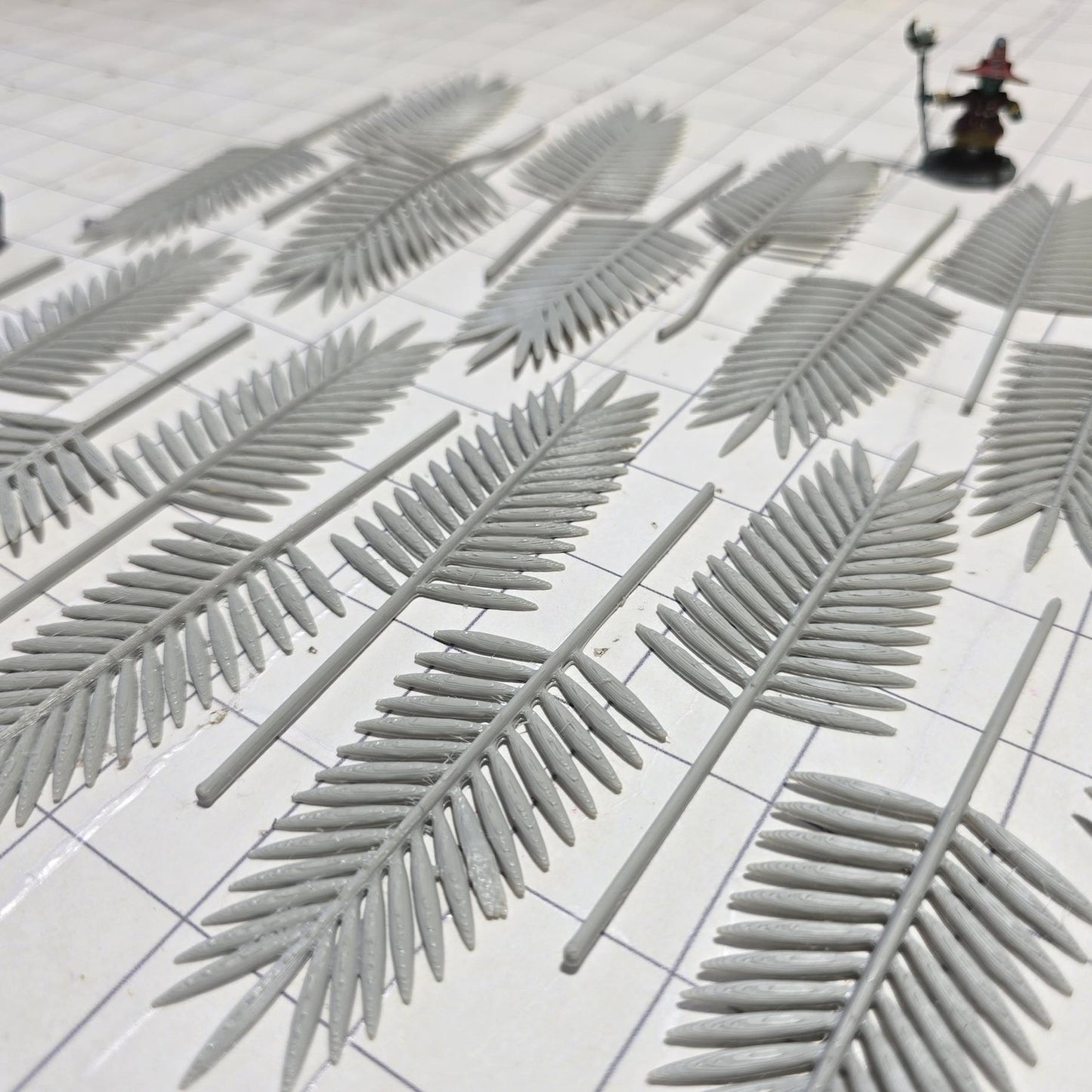 Laid across a 1" grid, these 28mm-scale palm fronds form a tropical spread waiting to be shaped and painted. With identical sprigs that bend under heat, they’re perfect for scratch-building palm trees, decorating temple ruins, or fleshing out dense jungle scenes. A miniature wizard and dice provide a sense of scale, highlighting their table-ready size.