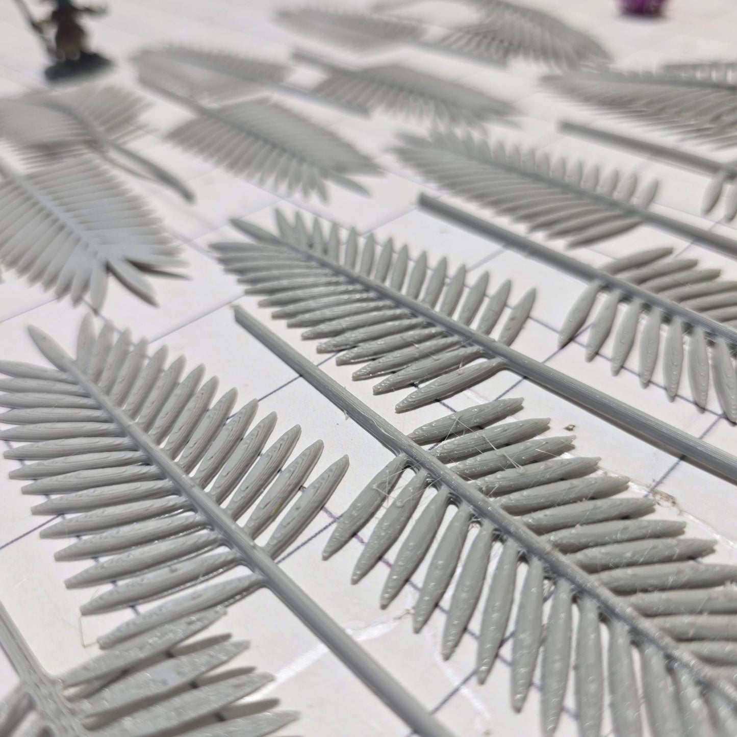 Laid across a 1" grid, these 28mm-scale palm fronds form a tropical spread waiting to be shaped and painted. With identical sprigs that bend under heat, they’re perfect for scratch-building palm trees, decorating temple ruins, or fleshing out dense jungle scenes. A miniature wizard and dice provide a sense of scale, highlighting their table-ready size.