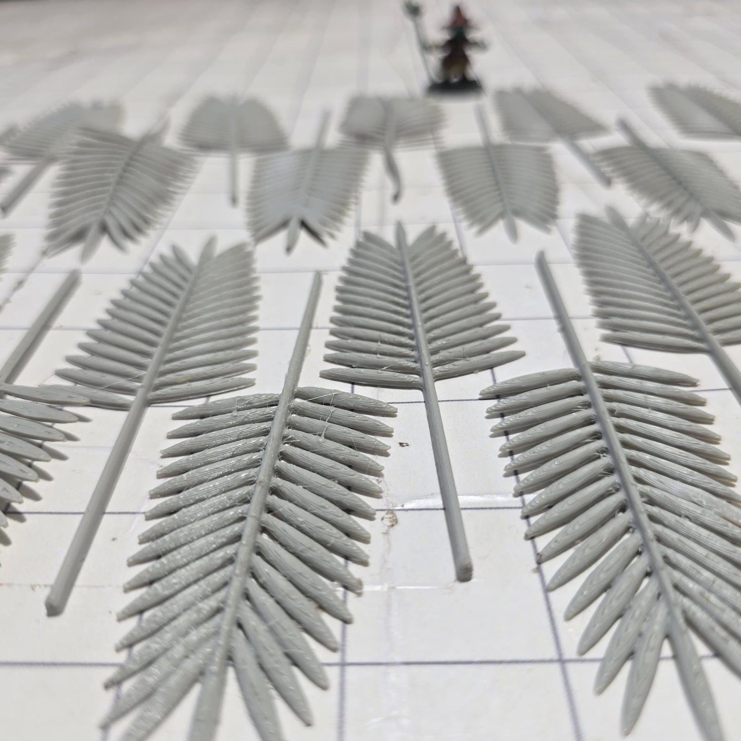 Laid across a 1" grid, these 28mm-scale palm fronds form a tropical spread waiting to be shaped and painted. With identical sprigs that bend under heat, they’re perfect for scratch-building palm trees, decorating temple ruins, or fleshing out dense jungle scenes. A miniature wizard and dice provide a sense of scale, highlighting their table-ready size.