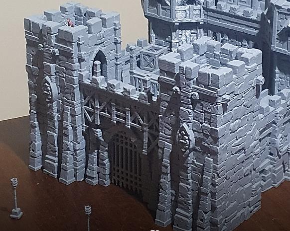 The Main Gate of the Kingdom of Guardia rises with twin towers and a heavy portcullis, ready to repel invaders or welcome wary travelers. Miniatures can be placed on the battlements or at the gate below, setting the stage for sieges, defenses, and dramatic encounters.