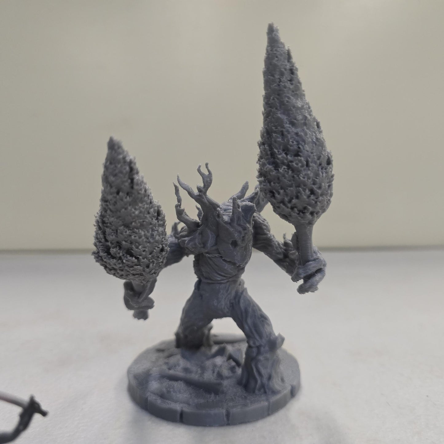 This large-scale Mossfang the Rootbreaker forest ent miniature is 3D printed in gray PLA and scaled for 28mm tabletop gaming. Standing nearly three times taller than standard humanoid miniatures, Mossfang grips two uprooted trees as weapons and features detailed bark textures, root-covered base detailing, and a wide stance for dramatic tabletop presence.
