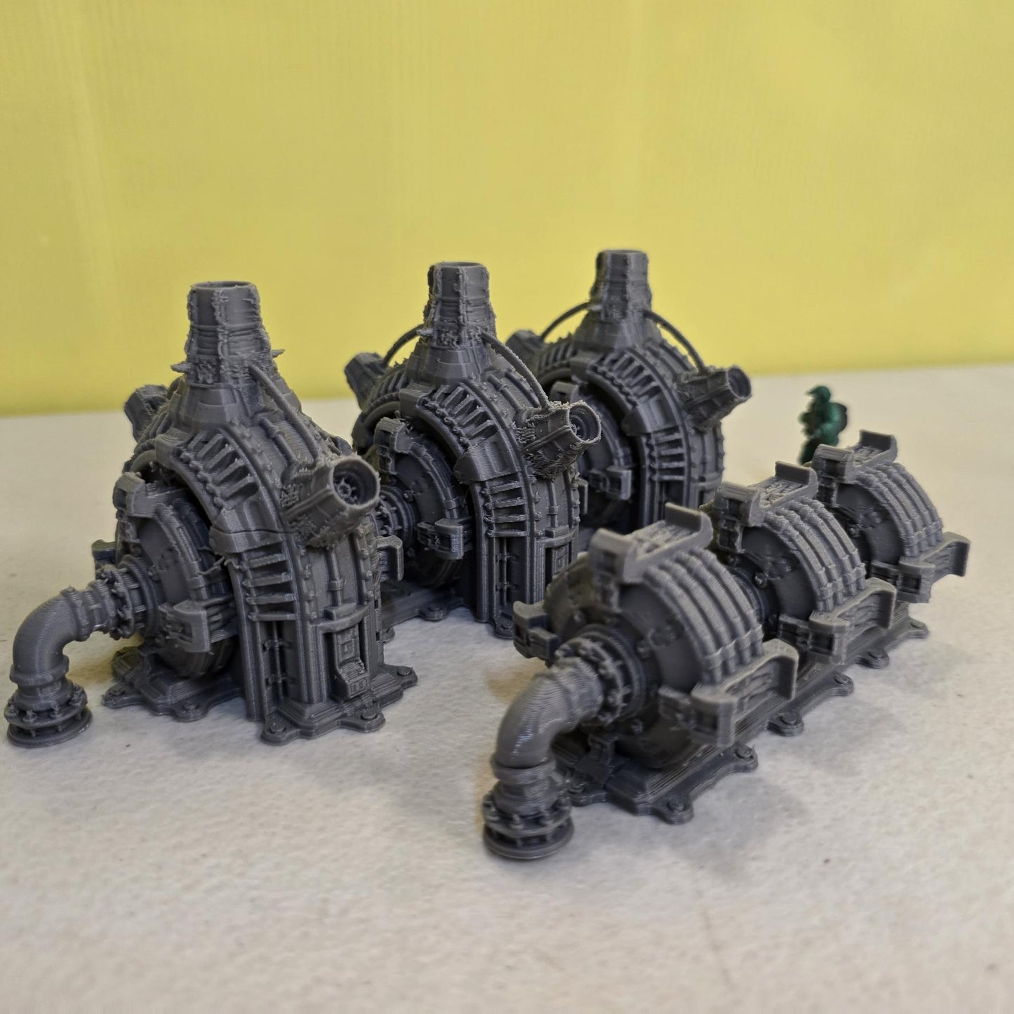 Grimdark power generator cells with ribbed housings, arched industrial frames, vent stacks, and curved pipe connections. Scaled for DnD / Pathfinder / wargaming. Miniatures and a D20 to show their footprint on a 1-inch grid. Several variants appear as single units and linked multi-cell arrays, giving the set the look of a dense industrial power system. Built as sci-fi scatter terrain, these generator cells bring heavy mechanical detail and battlefield atmosphere to any tabletop terrain layout.