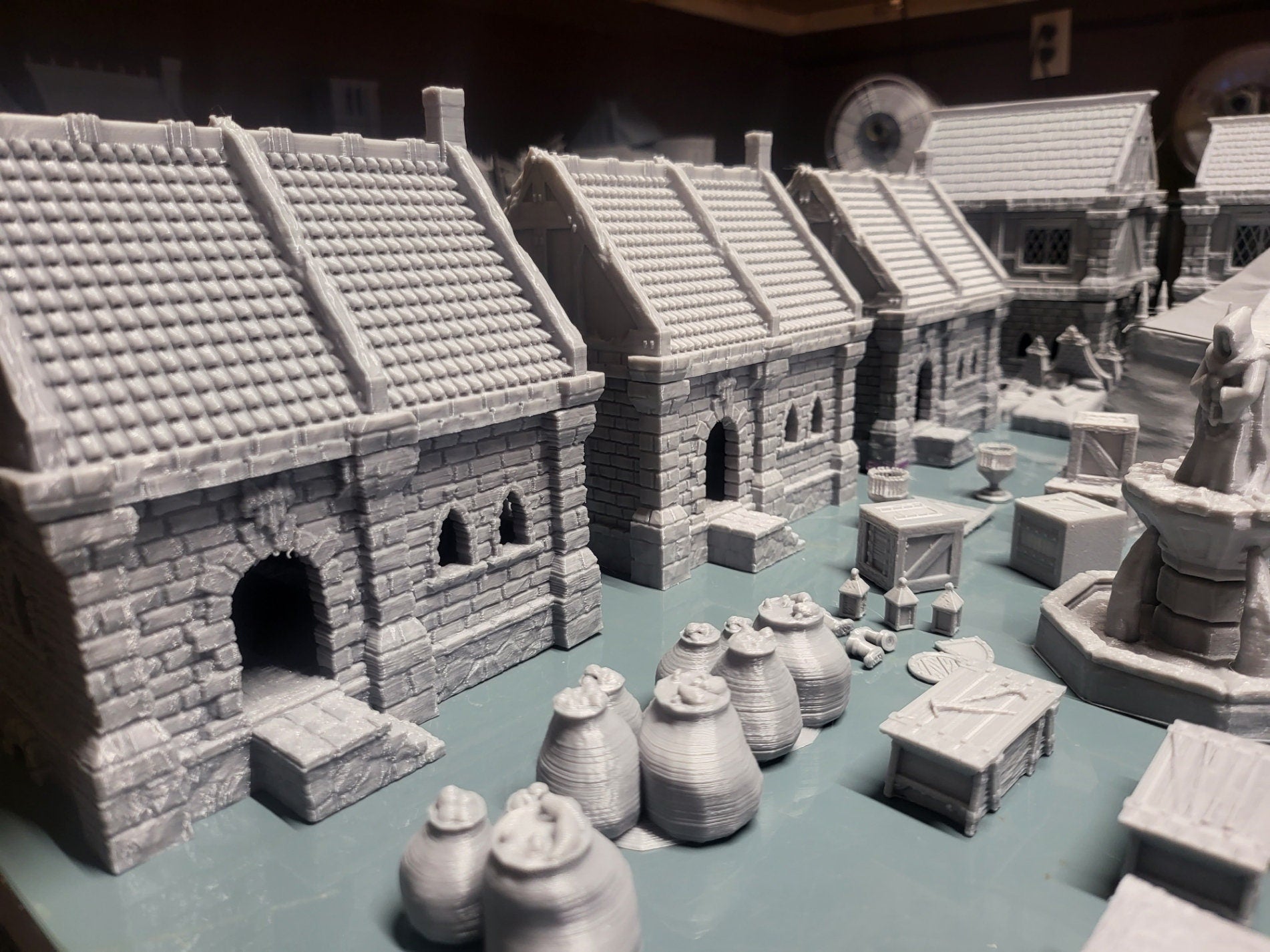 Set of 10 detailed 28mm buildings for tabletop RPGs, featuring wooden and stone structures with varied roof styles. Includes market wares and scatter terrain like barrels and crates. Perfect for village scenes in D&D, Pathfinder, and Warhammer.