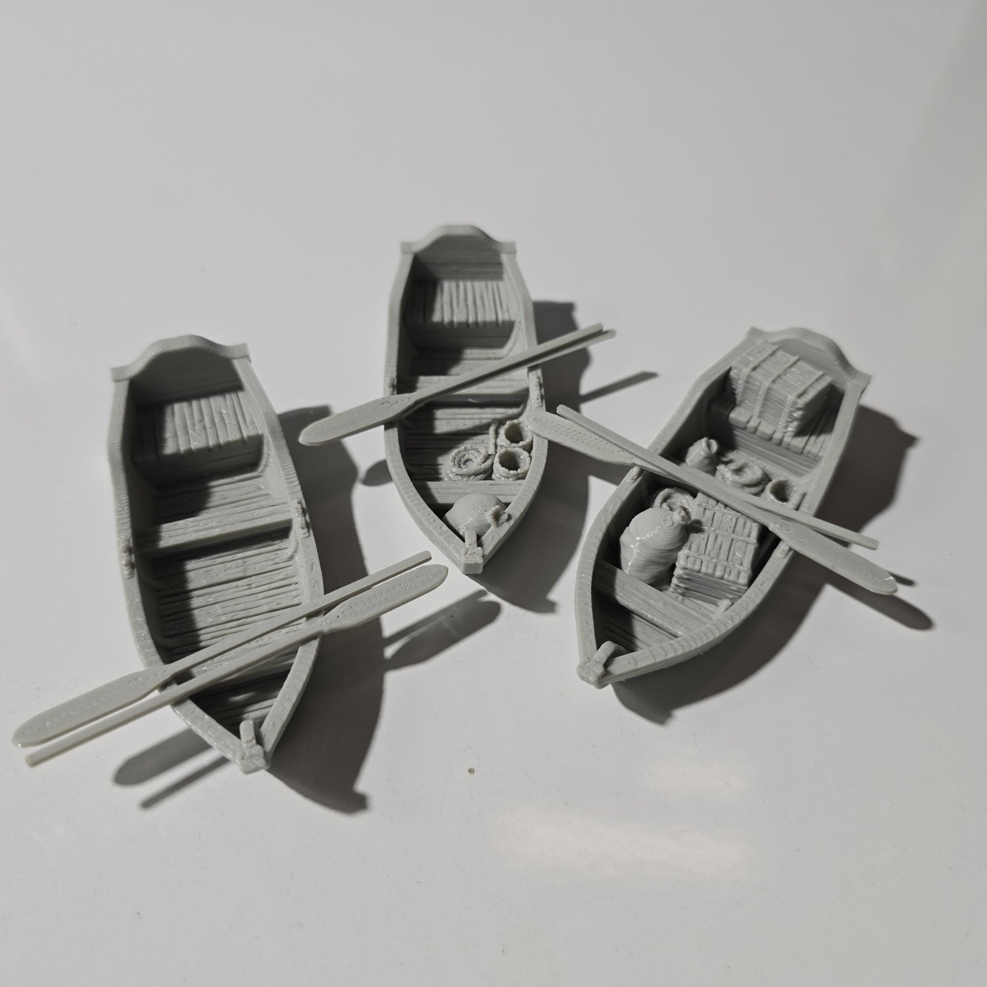 Set of 3 medieval rowboats with crates, barrels, sacks, ropes, and oars. Available in 15mm, 28mm, and 32mm scales—perfect for docks, rivers, and coastal scenes in fantasy and historical tabletop games.