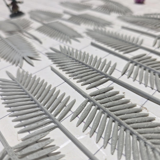 Laid across a 1&quot; grid, these 28mm-scale palm fronds form a tropical spread waiting to be shaped and painted. With identical sprigs that bend under heat, they’re perfect for scratch-building palm trees, decorating temple ruins, or fleshing out dense jungle scenes. A miniature wizard and dice provide a sense of scale, highlighting their table-ready size.