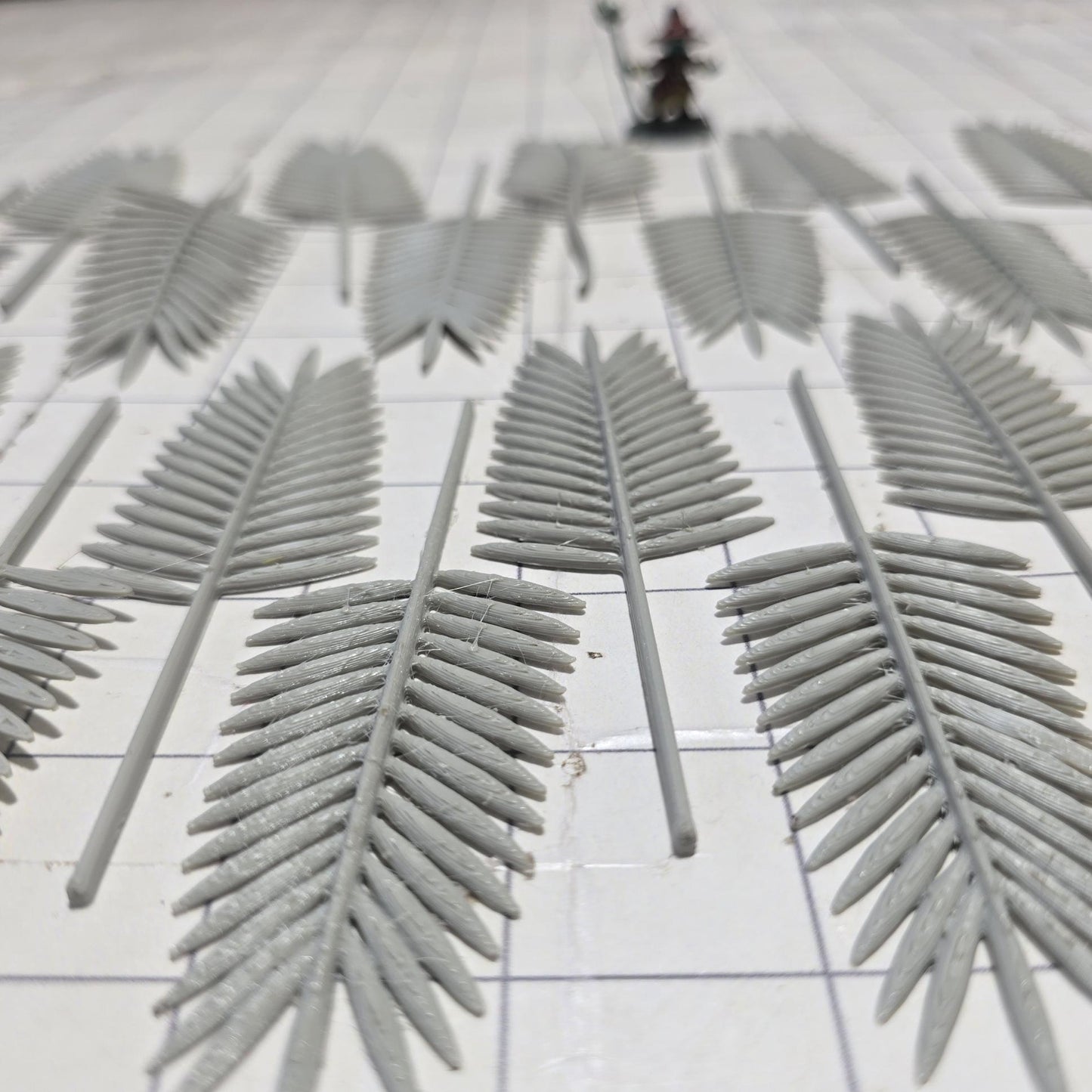 Laid across a 1&quot; grid, these 28mm-scale palm fronds form a tropical spread waiting to be shaped and painted. With identical sprigs that bend under heat, they’re perfect for scratch-building palm trees, decorating temple ruins, or fleshing out dense jungle scenes. A miniature wizard and dice provide a sense of scale, highlighting their table-ready size.