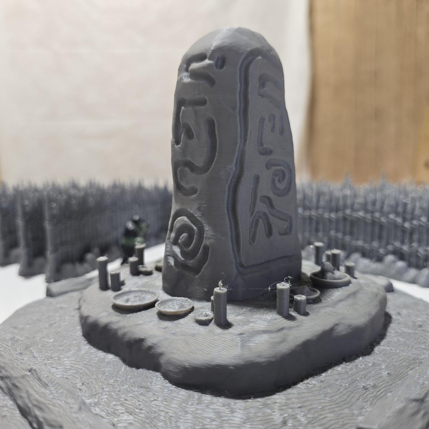 Unpainted gray PLA captures the rough ground, carved runestone, and jagged timber spikes of this 28 mm tabletop terrain set. The monolith rises from a layered base scattered with simple offerings, while the spiked walls form a full circle around the site. Each piece shows the subtle lines of 3D printed construction, ready for primer. Designed for DnD / Pathfinder / wargaming on a 1-inch grid, it stands as a stark landmark on any table.
