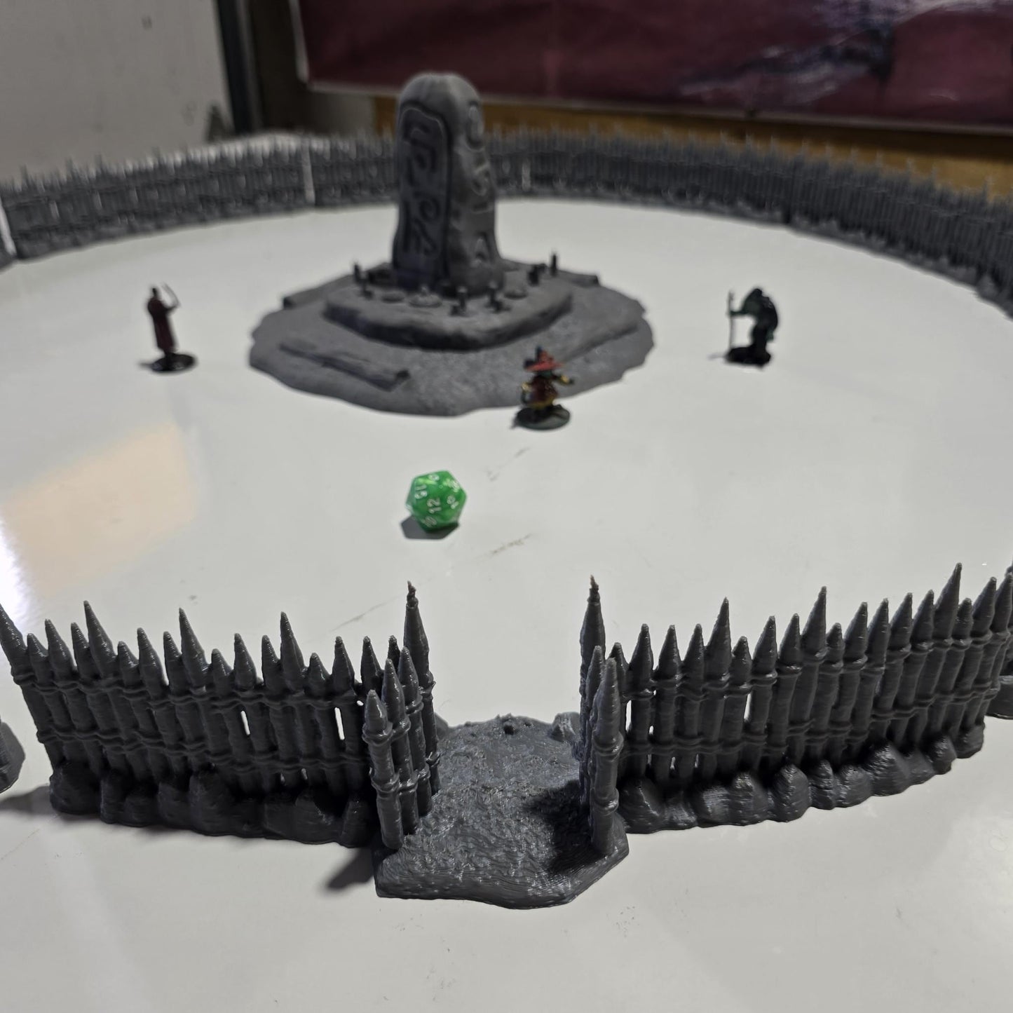 Unpainted gray PLA captures the rough ground, carved runestone, and jagged timber spikes of this 28 mm tabletop terrain set. The monolith rises from a layered base scattered with simple offerings, while the spiked walls form a full circle around the site. Each piece shows the subtle lines of 3D printed construction, ready for primer. Designed for DnD / Pathfinder / wargaming on a 1-inch grid, it stands as a stark landmark on any table.