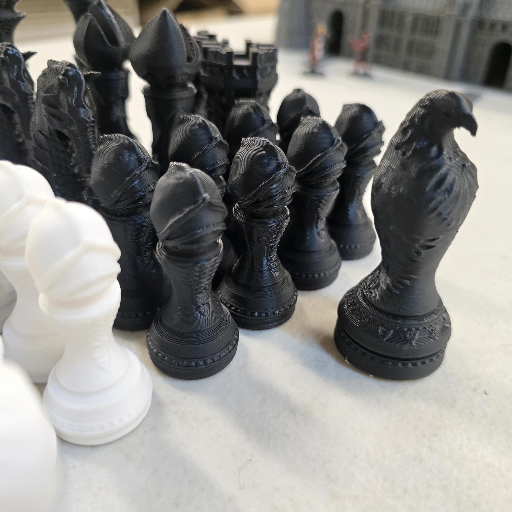 Close-up of black and white 3D printed chess pieces including sculpted raven piece and textured pawns from Royal Battle Board castle chess set