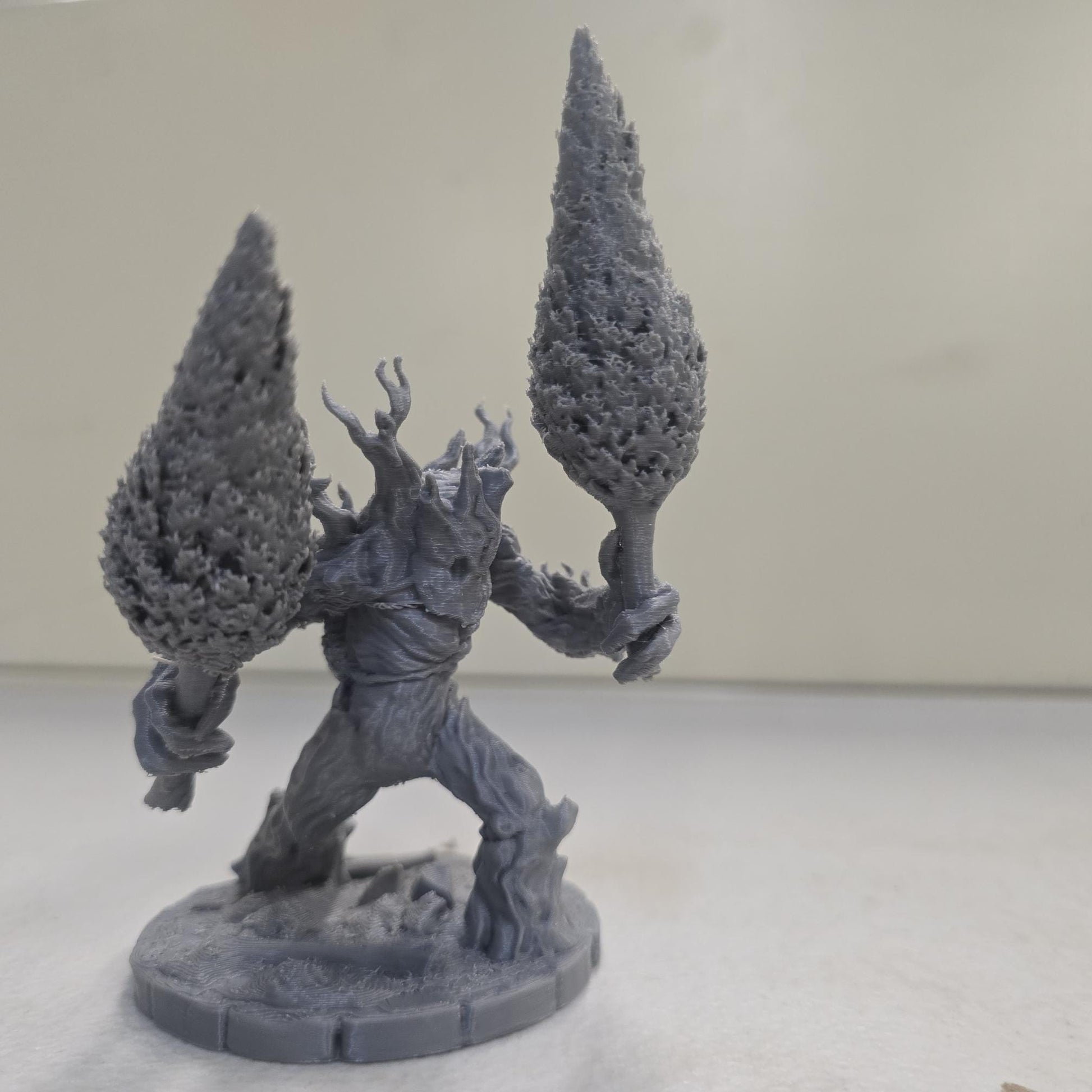 This large-scale Mossfang the Rootbreaker forest ent miniature is 3D printed in gray PLA and scaled for 28mm tabletop gaming. Standing nearly three times taller than standard humanoid miniatures, Mossfang grips two uprooted trees as weapons and features detailed bark textures, root-covered base detailing, and a wide stance for dramatic tabletop presence.