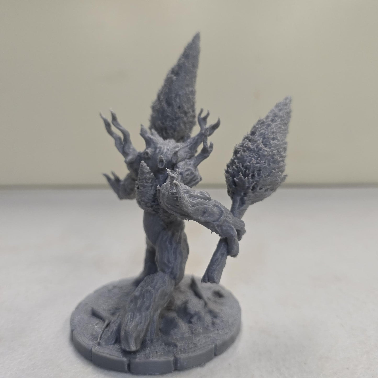 This large-scale Mossfang the Rootbreaker forest ent miniature is 3D printed in gray PLA and scaled for 28mm tabletop gaming. Standing nearly three times taller than standard humanoid miniatures, Mossfang grips two uprooted trees as weapons and features detailed bark textures, root-covered base detailing, and a wide stance for dramatic tabletop presence.