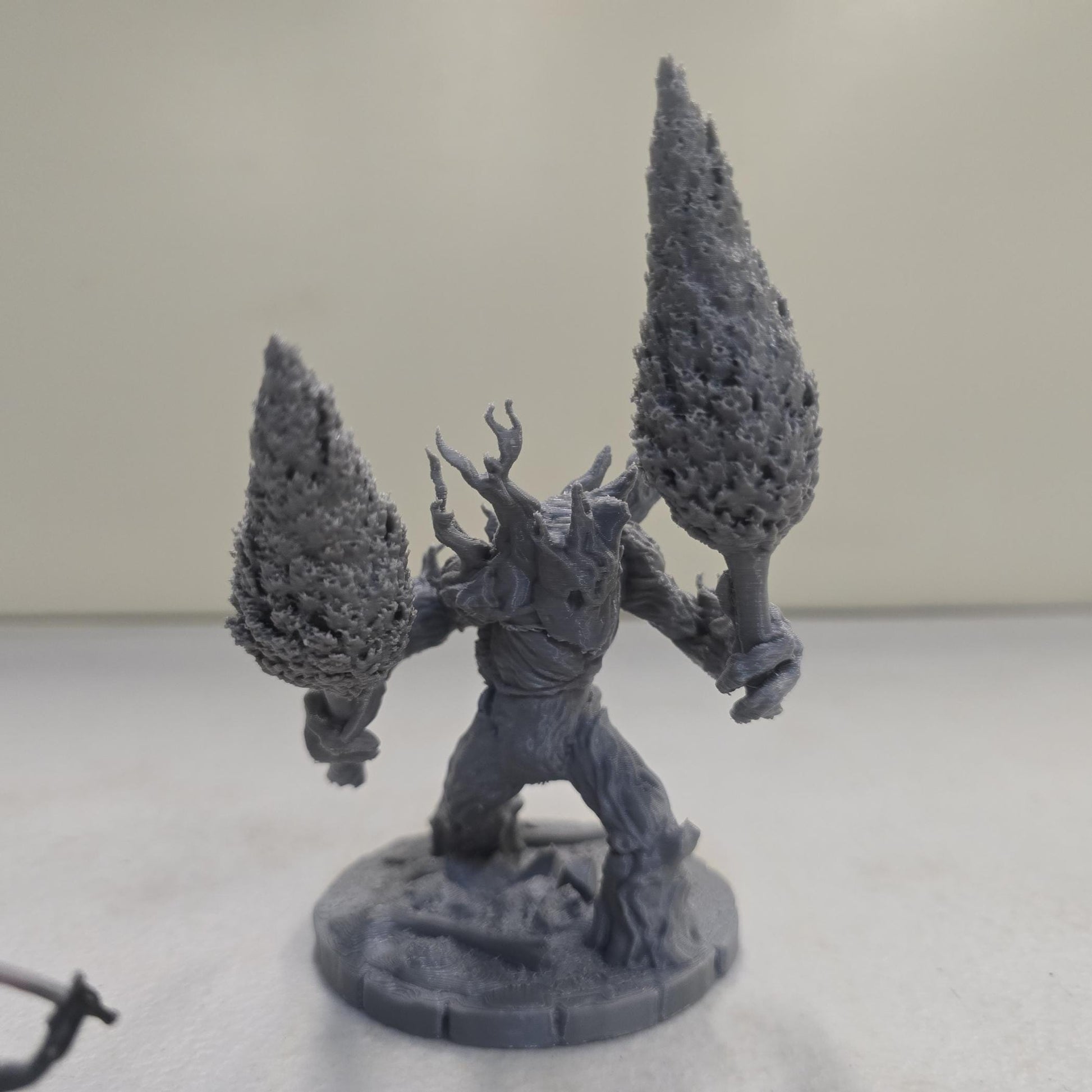 This large-scale Mossfang the Rootbreaker forest ent miniature is 3D printed in gray PLA and scaled for 28mm tabletop gaming. Standing nearly three times taller than standard humanoid miniatures, Mossfang grips two uprooted trees as weapons and features detailed bark textures, root-covered base detailing, and a wide stance for dramatic tabletop presence.