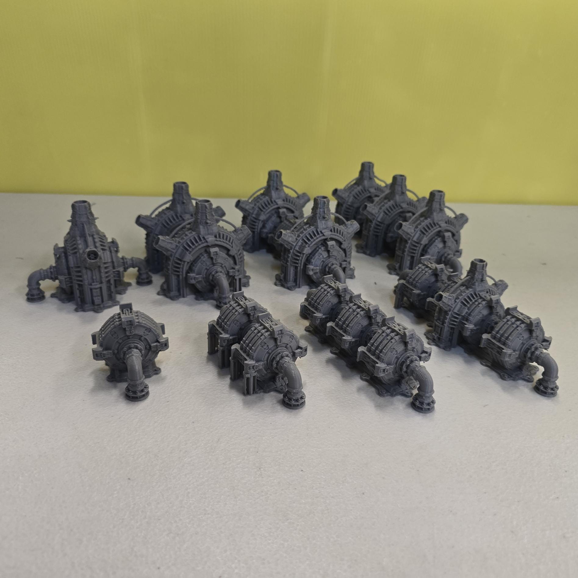 Grimdark power generator cells with ribbed housings, arched industrial frames, vent stacks, and curved pipe connections. Scaled for DnD / Pathfinder / wargaming. Miniatures and a D20 to show their footprint on a 1-inch grid. Several variants appear as single units and linked multi-cell arrays, giving the set the look of a dense industrial power system. Built as sci-fi scatter terrain, these generator cells bring heavy mechanical detail and battlefield atmosphere to any tabletop terrain layout.