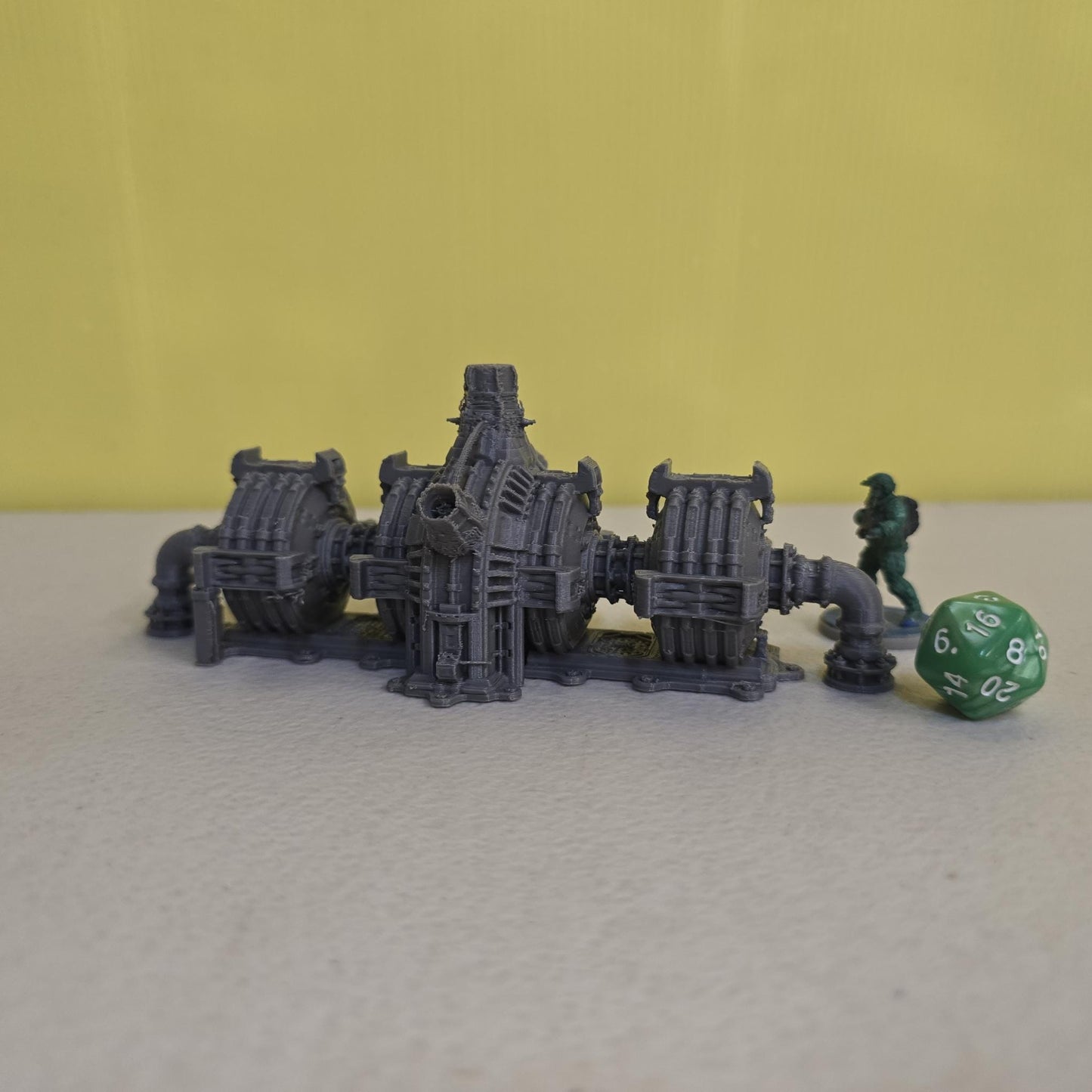 Grimdark power generator cells with ribbed housings, arched industrial frames, vent stacks, and curved pipe connections. Scaled for DnD / Pathfinder / wargaming. Miniatures and a D20 to show their footprint on a 1-inch grid. Several variants appear as single units and linked multi-cell arrays, giving the set the look of a dense industrial power system. Built as sci-fi scatter terrain, these generator cells bring heavy mechanical detail and battlefield atmosphere to any tabletop terrain layout.
