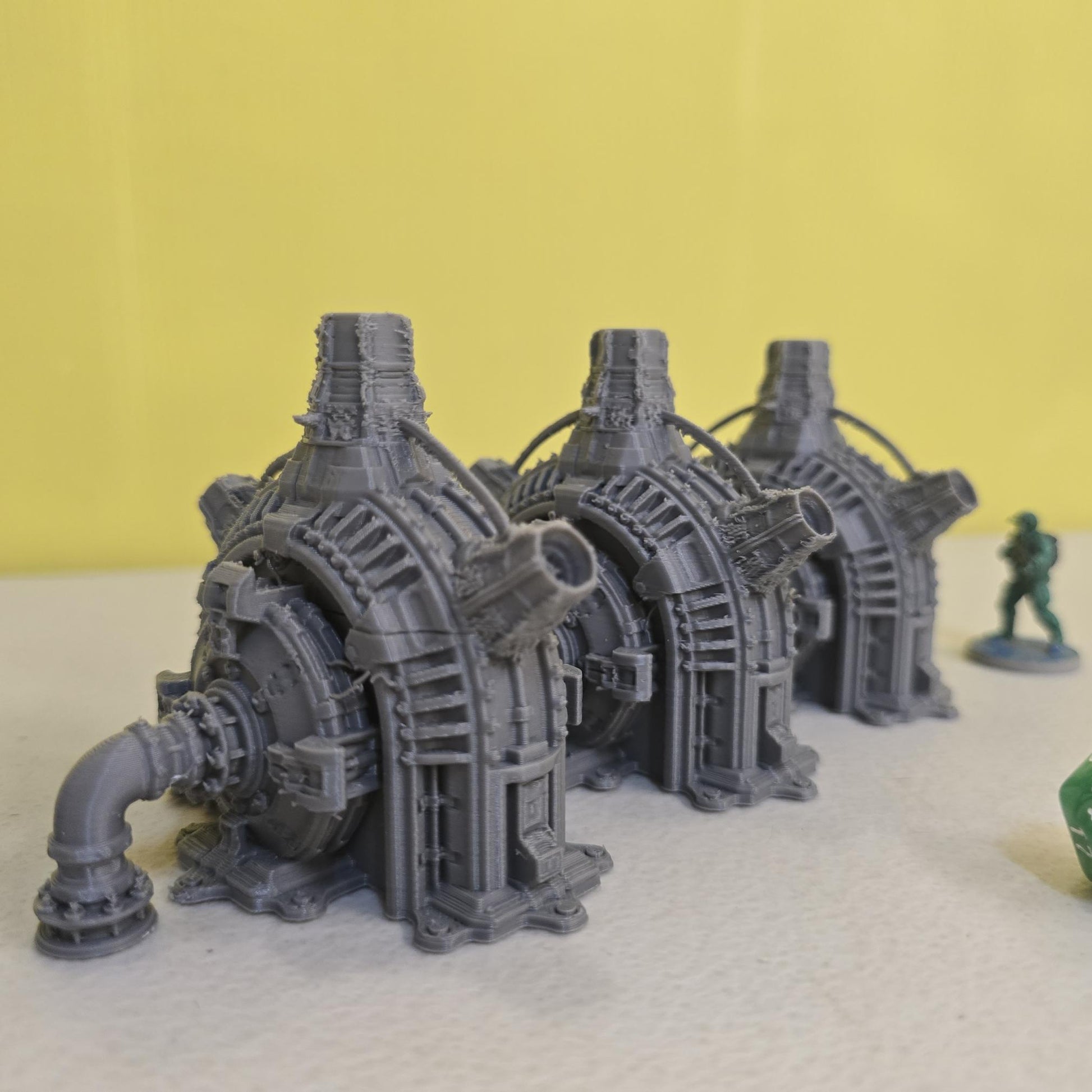 Grimdark power generator cells with ribbed housings, arched industrial frames, vent stacks, and curved pipe connections. Scaled for DnD / Pathfinder / wargaming. Miniatures and a D20 to show their footprint on a 1-inch grid. Several variants appear as single units and linked multi-cell arrays, giving the set the look of a dense industrial power system. Built as sci-fi scatter terrain, these generator cells bring heavy mechanical detail and battlefield atmosphere to any tabletop terrain layout.
