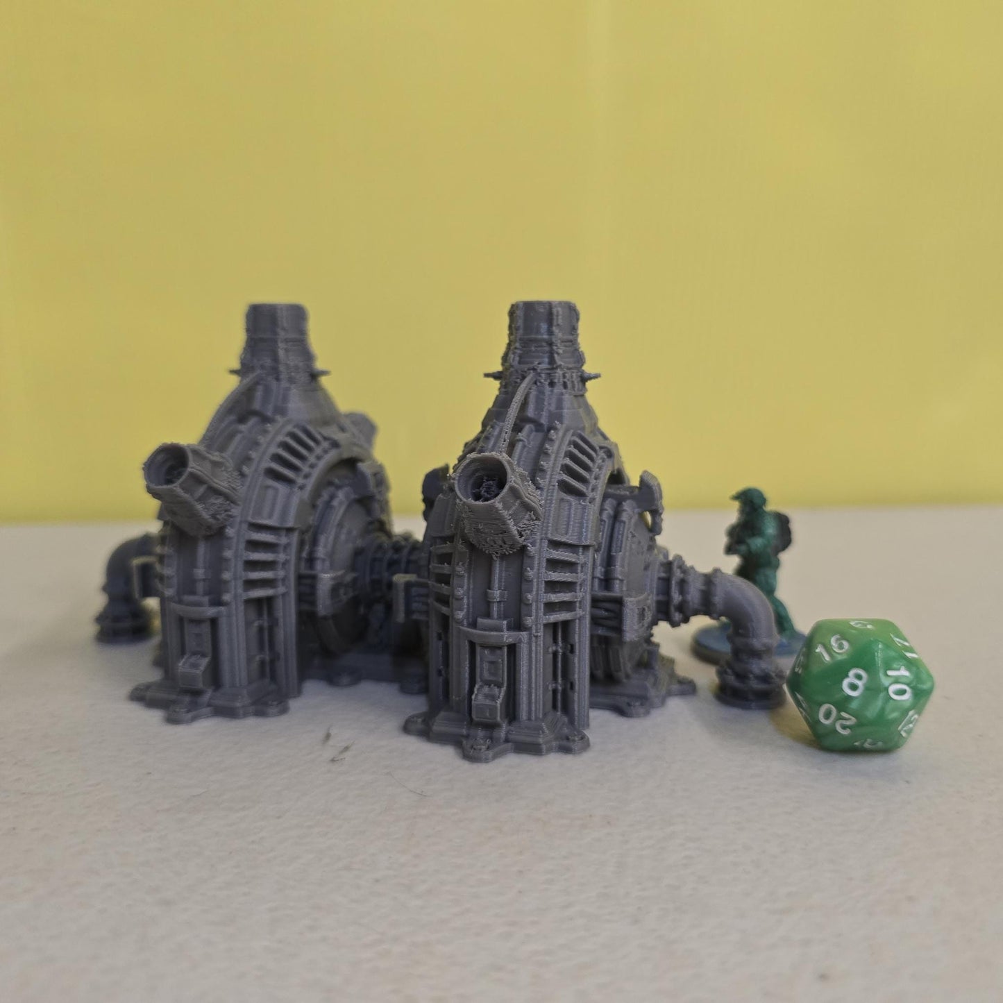 Grimdark power generator cells with ribbed housings, arched industrial frames, vent stacks, and curved pipe connections. Scaled for DnD / Pathfinder / wargaming. Miniatures and a D20 to show their footprint on a 1-inch grid. Several variants appear as single units and linked multi-cell arrays, giving the set the look of a dense industrial power system. Built as sci-fi scatter terrain, these generator cells bring heavy mechanical detail and battlefield atmosphere to any tabletop terrain layout.