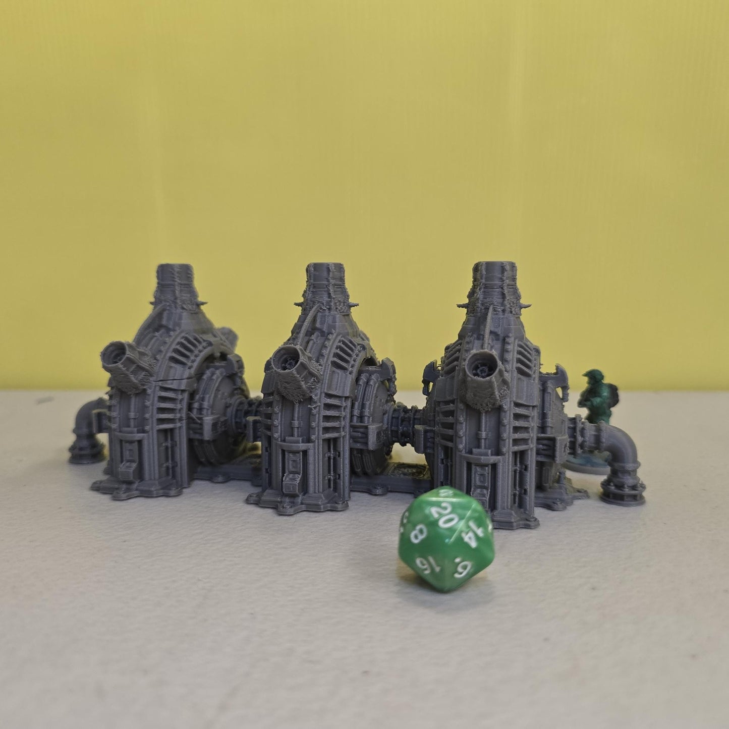 Grimdark power generator cells with ribbed housings, arched industrial frames, vent stacks, and curved pipe connections. Scaled for DnD / Pathfinder / wargaming. Miniatures and a D20 to show their footprint on a 1-inch grid. Several variants appear as single units and linked multi-cell arrays, giving the set the look of a dense industrial power system. Built as sci-fi scatter terrain, these generator cells bring heavy mechanical detail and battlefield atmosphere to any tabletop terrain layout.